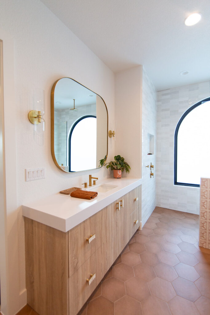 Five Oaks Custom Builders - custom renovated bathroom with accent mirror and arched window - tile accents and wooden textured storage