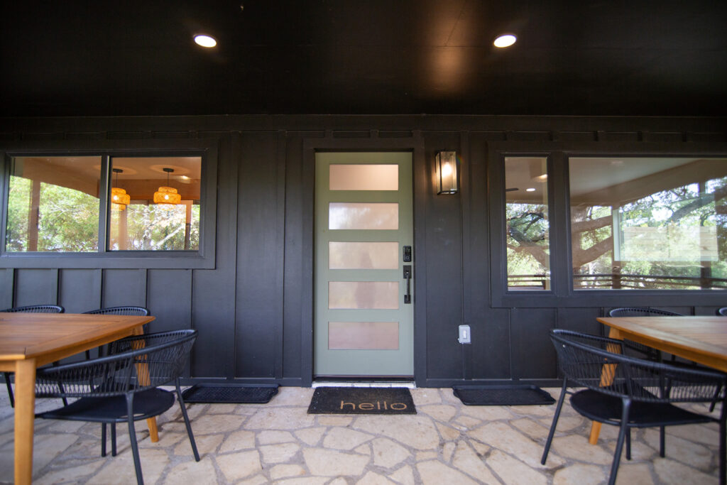 Five Oaks Custom Builders - dark painted wood home exterior with accent door, large windows, front porch seating for outdoor living area in Austin, Texas - central Texas, Leander